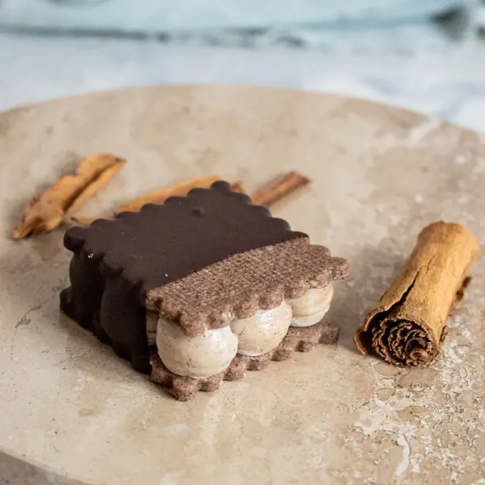 Chocolate-coated cinnamon vegan alfajor with cinnamon sticks