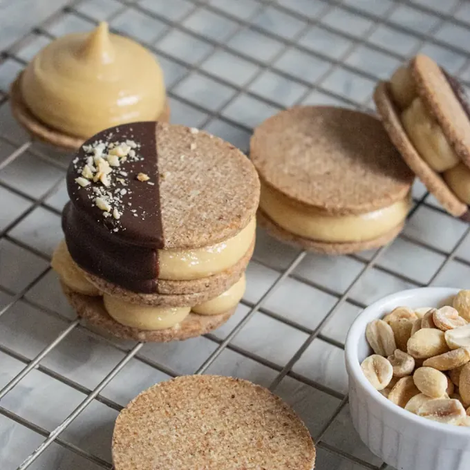 Peanut vegan alfajores on a cooling rack with roasted peanuts